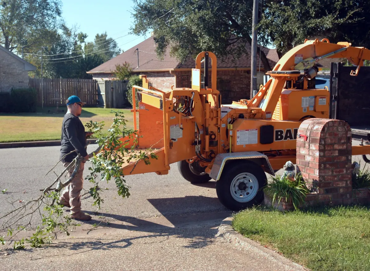 A tree service crew loading branches into a wood chipper in a residential driveway